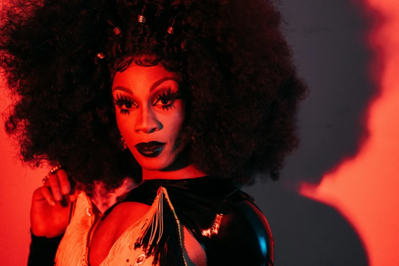 a woman with an afro posing for a picture, an album cover, trending on pexels, transgressive art, drag queen, lit from below with red lighting, hisoka, “wide shot