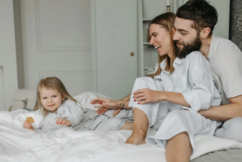 a man and woman sitting on a bed with a little girl, on the bed