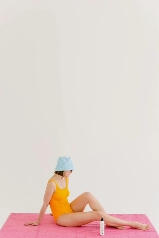 a woman sitting on top of a pink mat, by Lucette Barker, unsplash, visual art, in blue and yellow clothes, bucket hat, in white room, pale blue skin