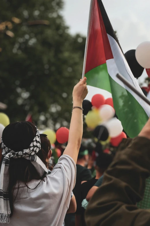 a group of people holding flags and balloons, a colorized photo, by Niko Henrichon, trending on unsplash, wearing a head scarf, closeup of fist, red green white black, israel