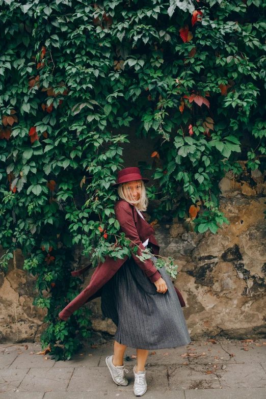 a little girl that is standing in front of a wall, inspired by Carl Larsson, unsplash contest winner, romanticism, maroon hat, woman made of plants, red tailcoat, with ivy