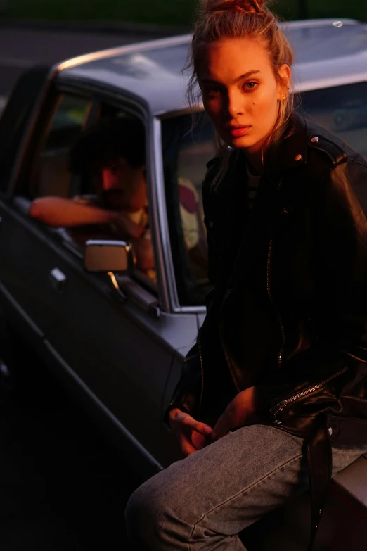 a woman sitting on the hood of a car, an album cover, inspired by Nan Goldin, trending on pexels, wearing samcrow leather jacket, promotional image, bella hadid, anders petersen