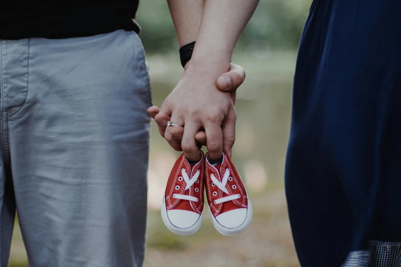 a close up of a person holding a pair of shoes, by Lucia Peka, pexels contest winner, symbolism, husband wife and son, pregnant belly, wearing red converse shoes, avatar image