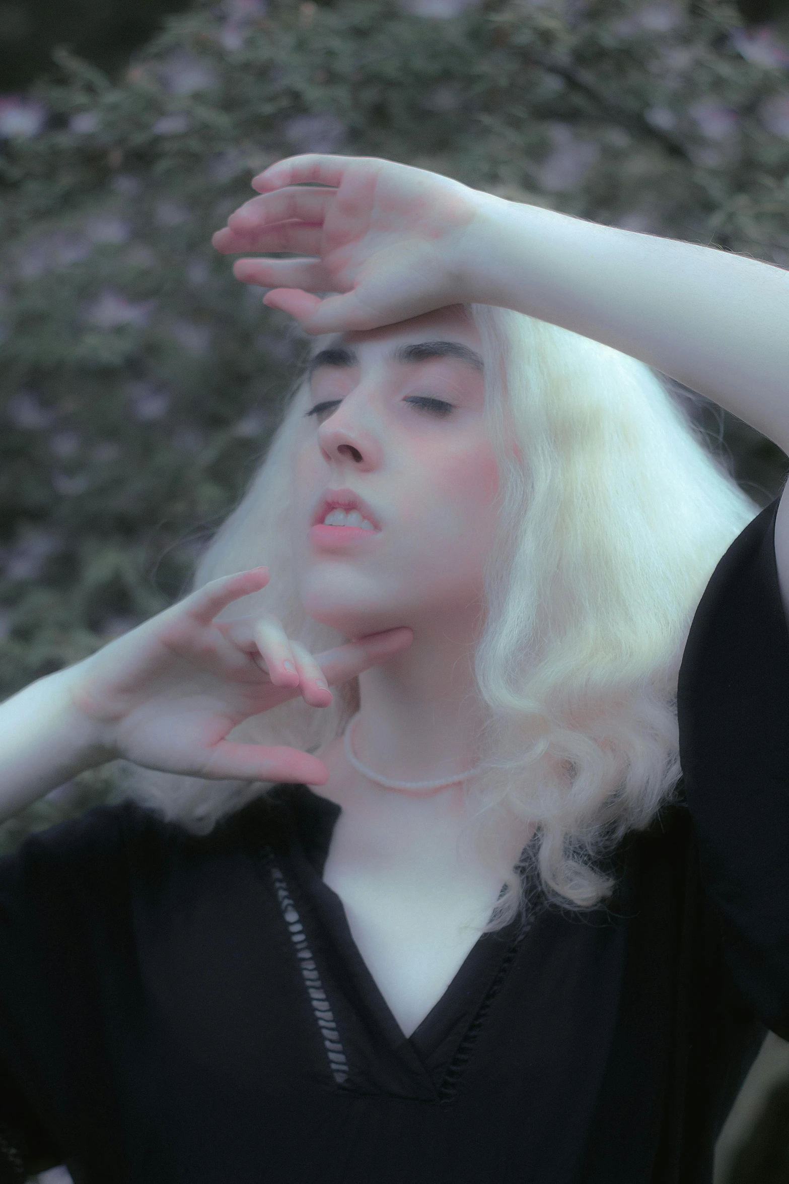 a woman standing in front of a tree with her hands on her head, an album cover, inspired by Elsa Bleda, unsplash, aestheticism, pale hair, intense albino, low quality footage, porcelain skin ”