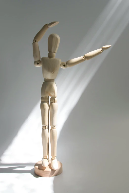 a wooden mannequin standing in front of a white wall, by David Simpson, visual art, arms outstretched, in a sunbeam, action figurine toy, bathed in light