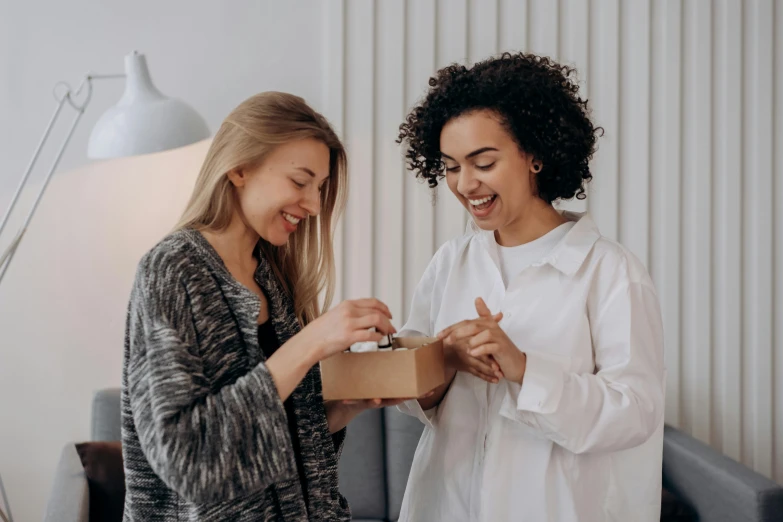 two women standing next to each other in a living room, by Eden Box, pexels contest winner, happening, earing a shirt laughing, giving gifts to people, avatar image, first aid kit