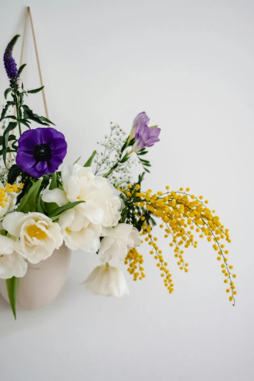 a white vase filled with purple and white flowers, yellow details, hanging, playful composition, in a white boho style studio