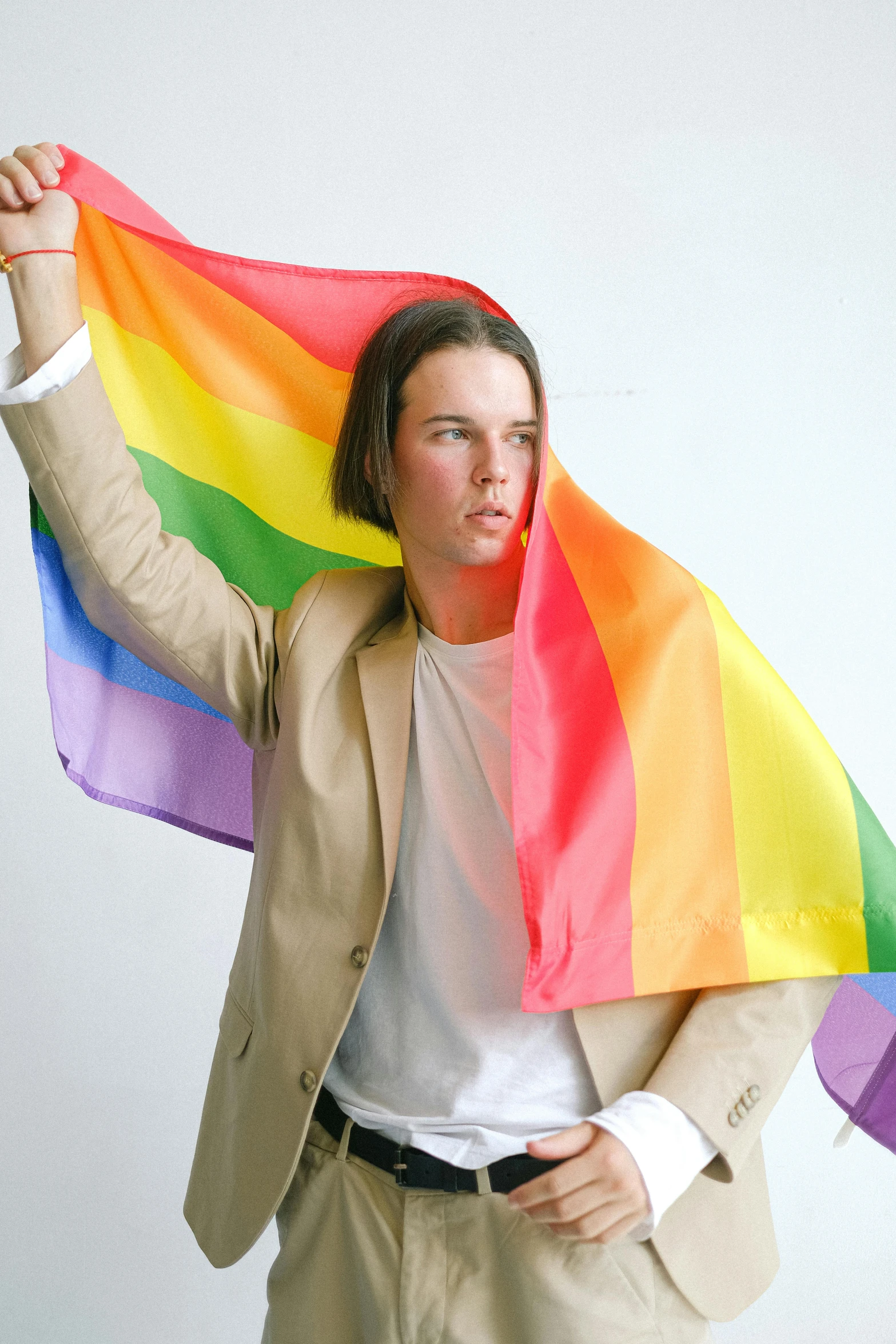 a man in a suit holding a rainbow flag, by Jessie Alexandra Dick, jamie campbell bower, on a pale background, sydney hanson, julian ope