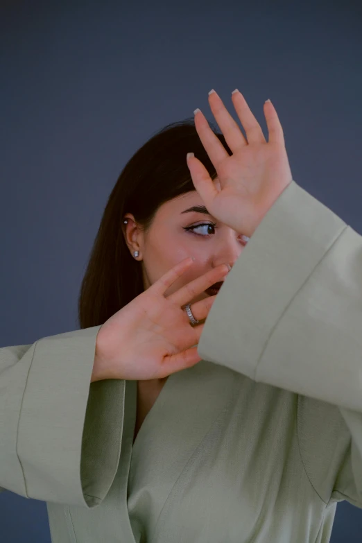 a woman covering her face with her hands, an album cover, by Attila Meszlenyi, wearing only a green robe, dabbing, on a gray background, headshot profile picture