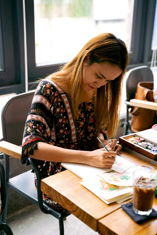 a woman sitting at a table writing on a piece of paper, a watercolor painting, crafts and souvenirs, studious, brown