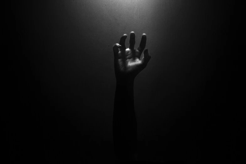 a black and white photo of a hand reaching for a light, pexels, symbolism, dark-skinned, album art, creepy black figure standing, dark studio light