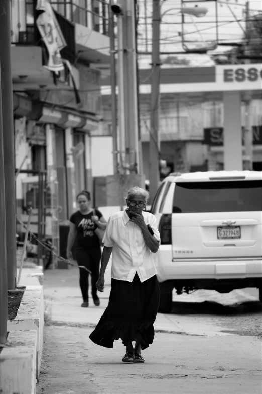 a man walking down a street talking on a cell phone, a black and white photo, by Yosa Buson, happening, he is a mad old man, henry ascensio, in town, :: morning