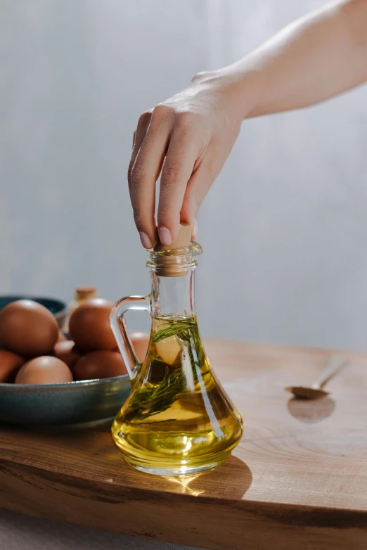 a person holding a bottle of olive oil next to a bowl of eggs, by Julia Pishtar, trending on pexels, renaissance, made of liquid, dynamic angled shot, petite, brown