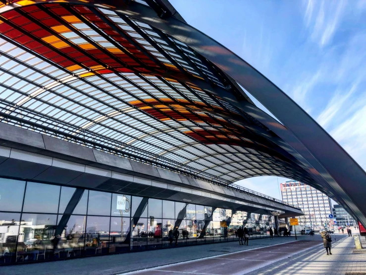 a group of people walking down a sidewalk next to a train station, inspired by Zaha Hadid, pexels contest winner, bauhaus, orange roof, black. airports, huge glass structure, view from the ground