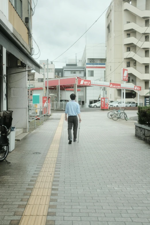 a man walking down a sidewalk next to a building, unsplash, shin hanga, accessible for the disabled, akihito tsukushi, cityscape, live action