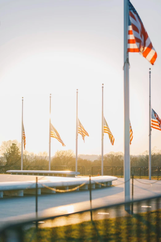 a row of american flags in front of a building, sunset in the distance, monuments, stanchions, sweeping vista