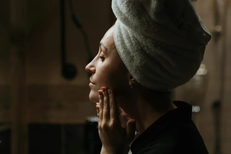 a woman with a towel wrapped around her head, trending on pexels, hyperrealism, right hand side profile, evening time, skincare, looking in a mirror