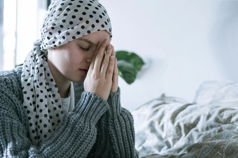 a woman sitting on a bed with her head in her hands, trending on pexels, hurufiyya, wearing cross on robe, wearing a head scarf, tumours, supportive