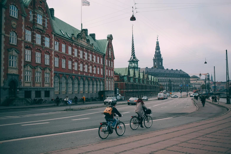 a couple of people riding bikes down a street, by Jesper Knudsen, pexels contest winner, red castle in background, square, bjarke ingels, schools