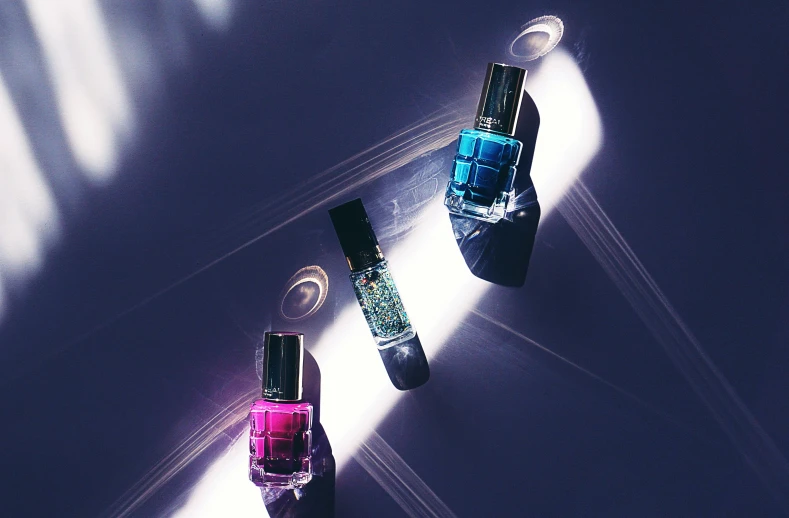 a couple of nail polish bottles sitting on top of a table, inspired by Évariste Vital Luminais, unsplash, photorealism, blue lights and purple lights, jewelled, 3 colours, shot with sony alpha