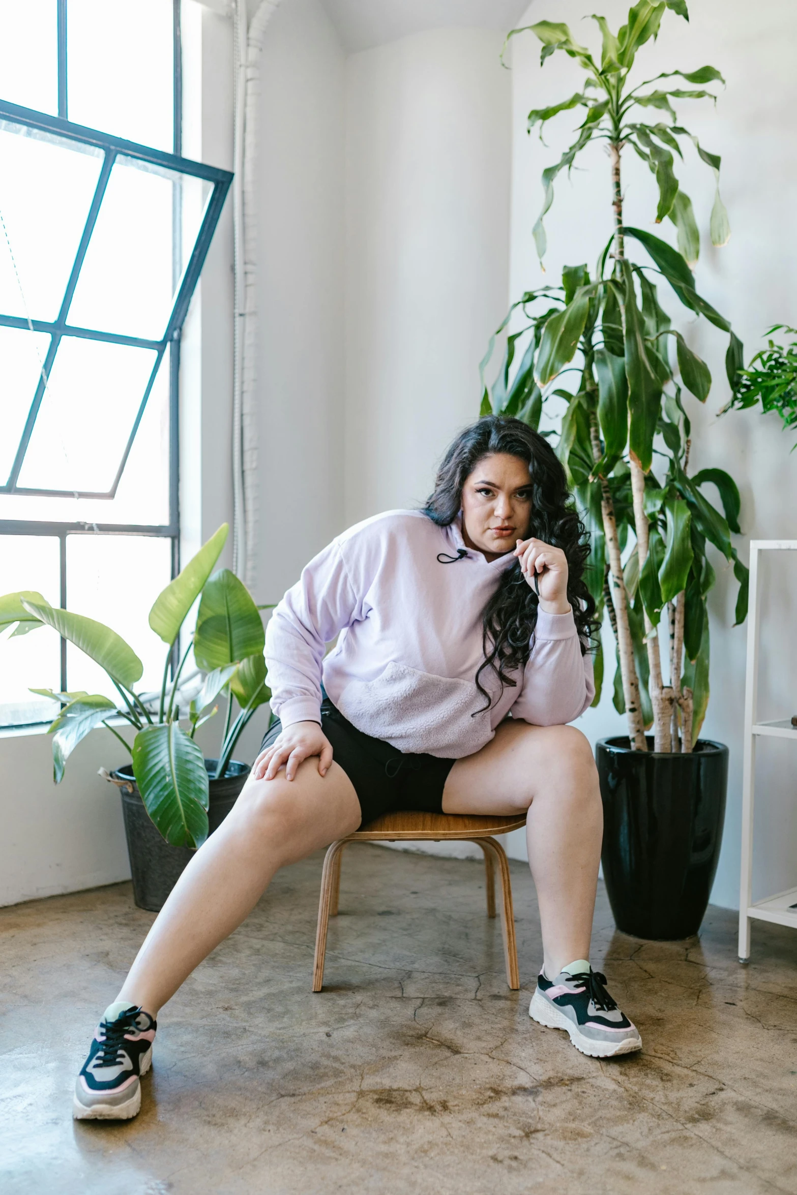 a woman sitting on a chair next to a potted plant, a portrait, unsplash, bra and shorts streetwear, fat woman, ((purple)), wearing sweatshirt