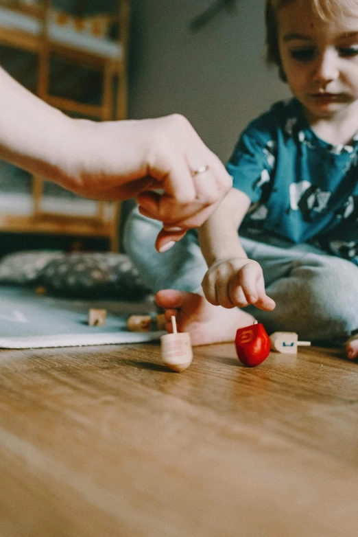 a small child sitting on the floor playing with a toy, by Sebastian Spreng, pexels contest winner, back of hand on the table, wooden magic wand, holding an apple, caretaker