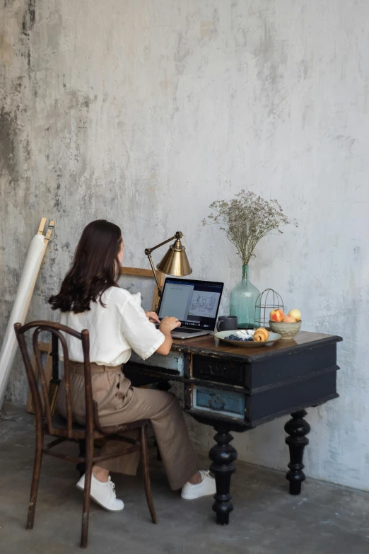 a woman sitting at a desk with a laptop, inspired by Juan Luna, pexels contest winner, studio setup, dwell, rustic, tall