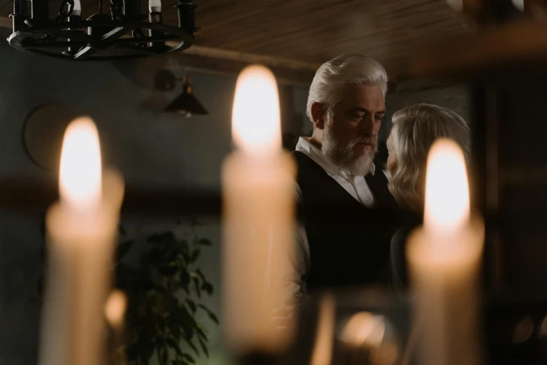 a man and a woman standing in front of a bunch of candles, white hair and white beard, cinematic soft lighting, profile image, a seance