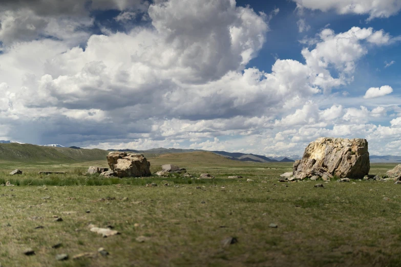 a herd of sheep grazing on top of a lush green field, by Alexander Runciman, unsplash, land art, bleak. big stones, mongolia, 3 6 0 panorama, cumulus