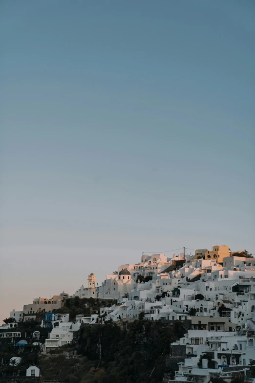 a hill covered in white buildings next to a body of water, by Alexis Grimou, trending on unsplash, cloudless sky, dawn, greek nose, low quality photo