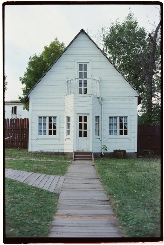 a white house sitting on top of a lush green field, a colorized photo, inspired by Isaac Levitan, folk art, white plank siding, front view 1 9 9 0, patagonian, museum setting