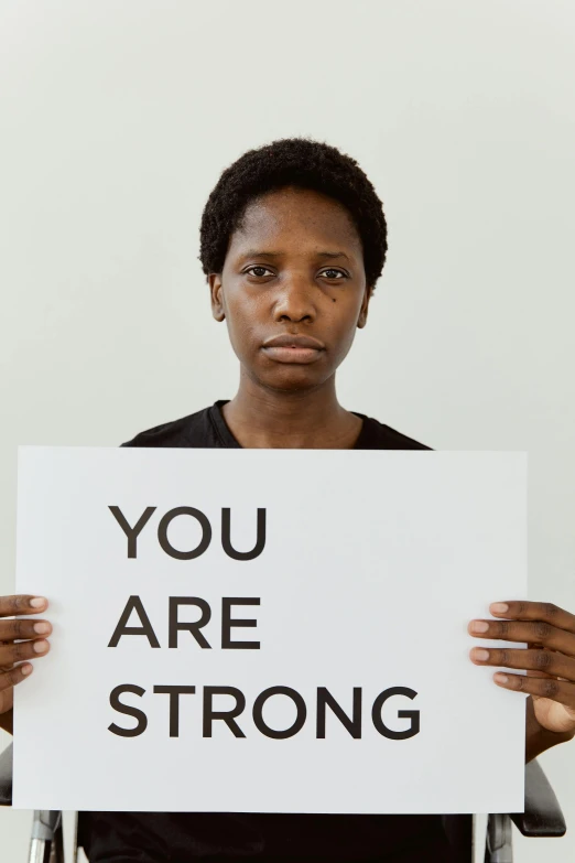 a woman holding a sign that says you are strong, a polaroid photo, edmonia lewis, david uzochukwu, ptsd, african woman