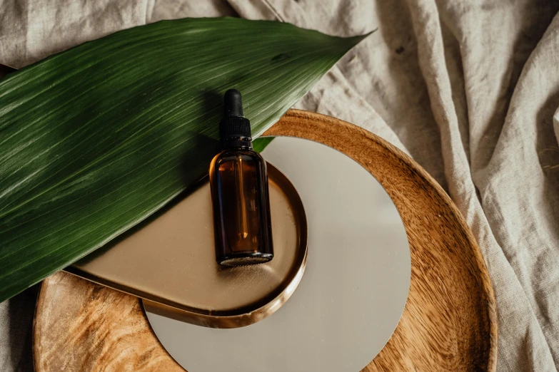 a bottle of essential oil sitting on top of a white plate, by Emma Andijewska, trending on pexels, renaissance, chest covered with palm leaves, sitting on a mocha-colored table, on a wooden plate, lacquer on canvas