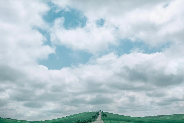 a man riding a motorcycle down a dirt road, an album cover, pexels contest winner, renaissance, sky full of clouds, on a green hill, minimalist photo, teal landscape