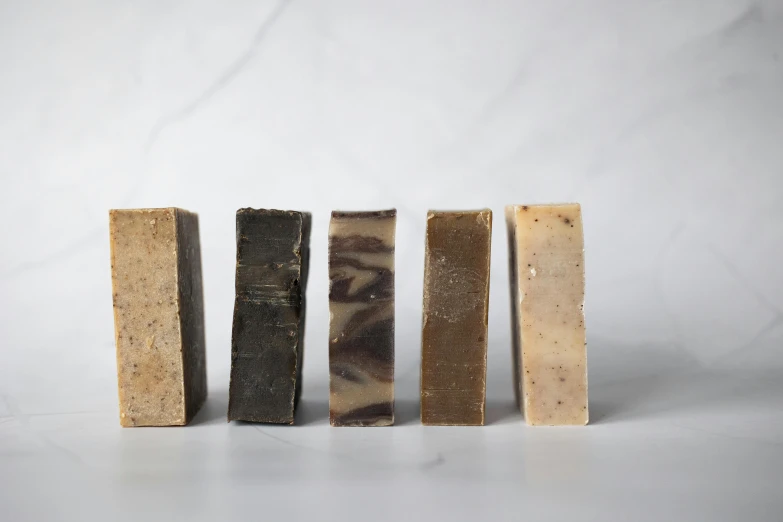 a group of soap bars sitting next to each other, by Emma Andijewska, chocolate. rugged, on a pale background, weathered olive skin, thumbnail