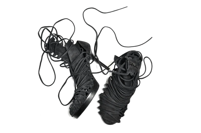 a pair of black shoes on a white surface, inspired by Slava Raškaj, cybernetic dreadlocks, tall gladiator sandals, carbon fibers, laces