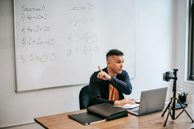 a man sitting at a table in front of a laptop, by Carey Morris, trending on unsplash, academic art, whiteboards, maths, two buddies sitting in a room, lachlan bailey