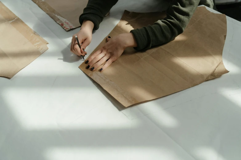 a person cutting paper with scissors on a table, brown clothes, unframed, modelling, aesthetically pleasing