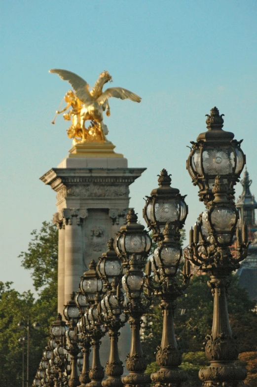 a group of street lamps sitting next to each other, a statue, inspired by Édouard Detaille, neoclassicism, gold wings on head, bridge, golden dappled lighting, parapets