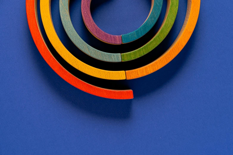 a close up of a circular object on a blue surface, an abstract sculpture, inspired by Jan Rustem, trending on pexels, op art, rainbow, wooden jewerly, five planets, arcs