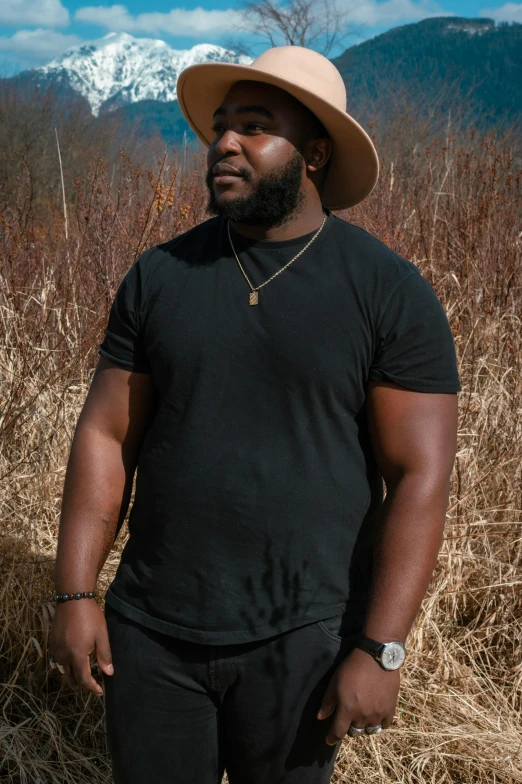 a man in a hat standing in a field, an album cover, by Nyuju Stumpy Brown, pexels contest winner, alluring plus sized model, he is wearing a black t-shirt, ( ( dark skin ) ), profile pic