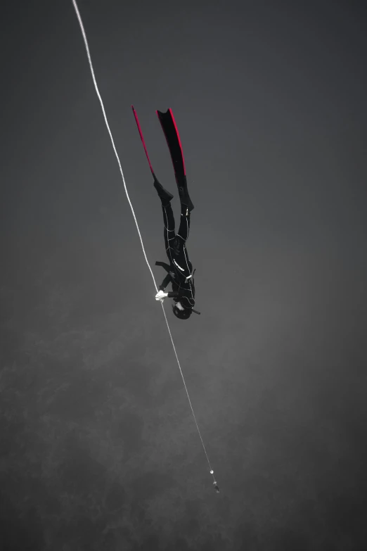 a person that is in the water with a kite, black undersuit, looking down from above, black and white and red, hanging cables