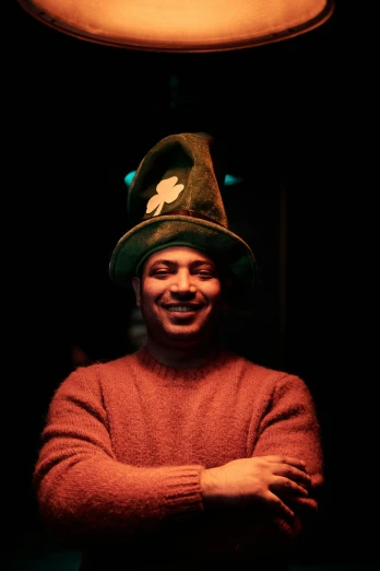 a man wearing a green hat in a dark room, an album cover, inspired by Luigi Kasimir, reddit, happy and spirited expression, thiago alcantara, jester hat, in a pub