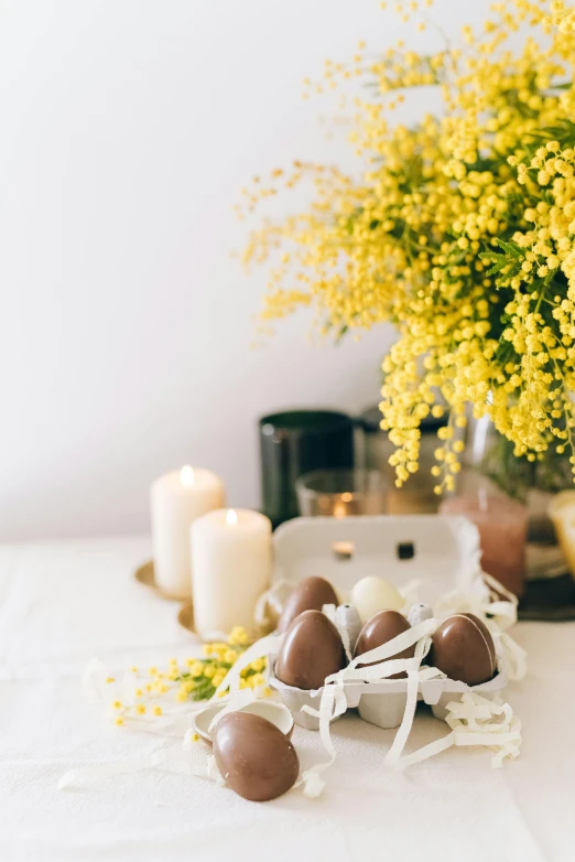 a bunch of eggs sitting on top of a table, white candles, with yellow flowers around it, fully chocolate, australian