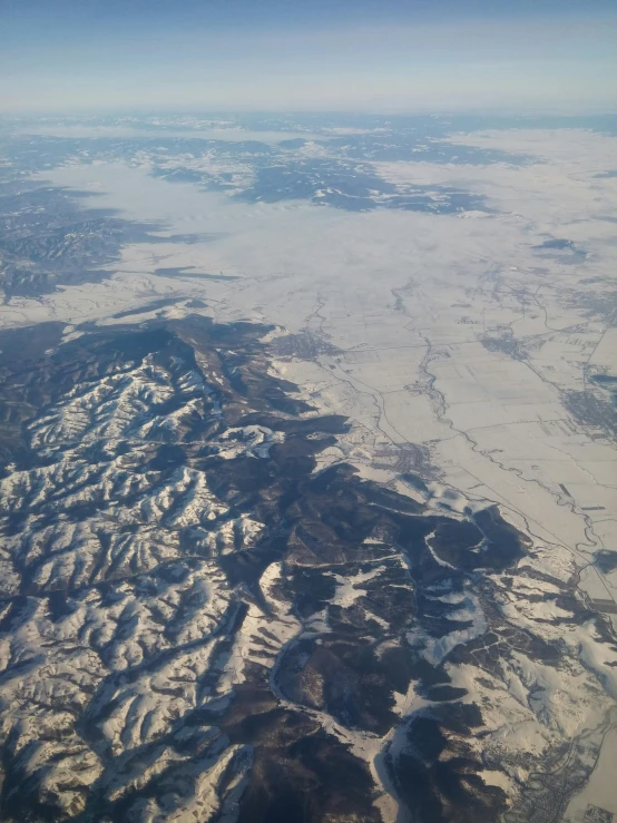 an aerial view of a snow covered mountain range, earth in the distance, split near the left, frozen and covered in ice, thumbnail