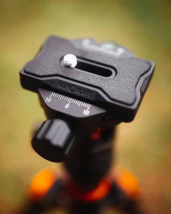 a close up of a camera on a tripod, dark grey and orange colours, phantom grip, easy to use, colour corrected