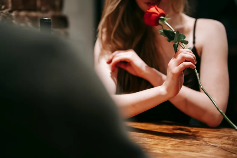 a woman sitting at a table with a rose in her hand, trending on pexels, making out, lesbians, sydney hanson, late evening