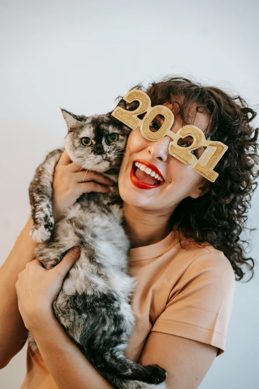 a woman holding a cat in front of her face, trending on pexels, happening, new years eve, a still of a happy, cardboard cutout, curly haired