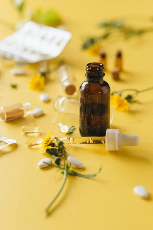 a bottle of medicine sitting on top of a table, by Andries Stock, trending on pexels, renaissance, yellow flowers, yellow backdrop, surgical iv drip, natural skin