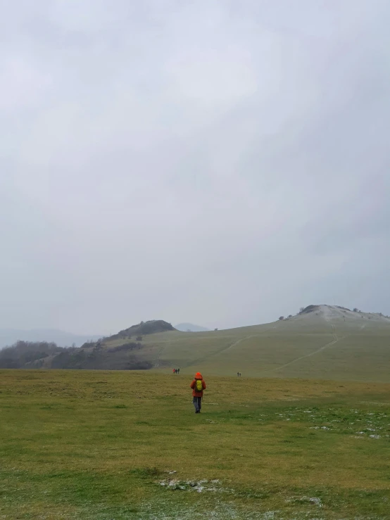 a person in a field flying a kite, on the top of a hill, grey skies rain, catacomb in background, roman nose